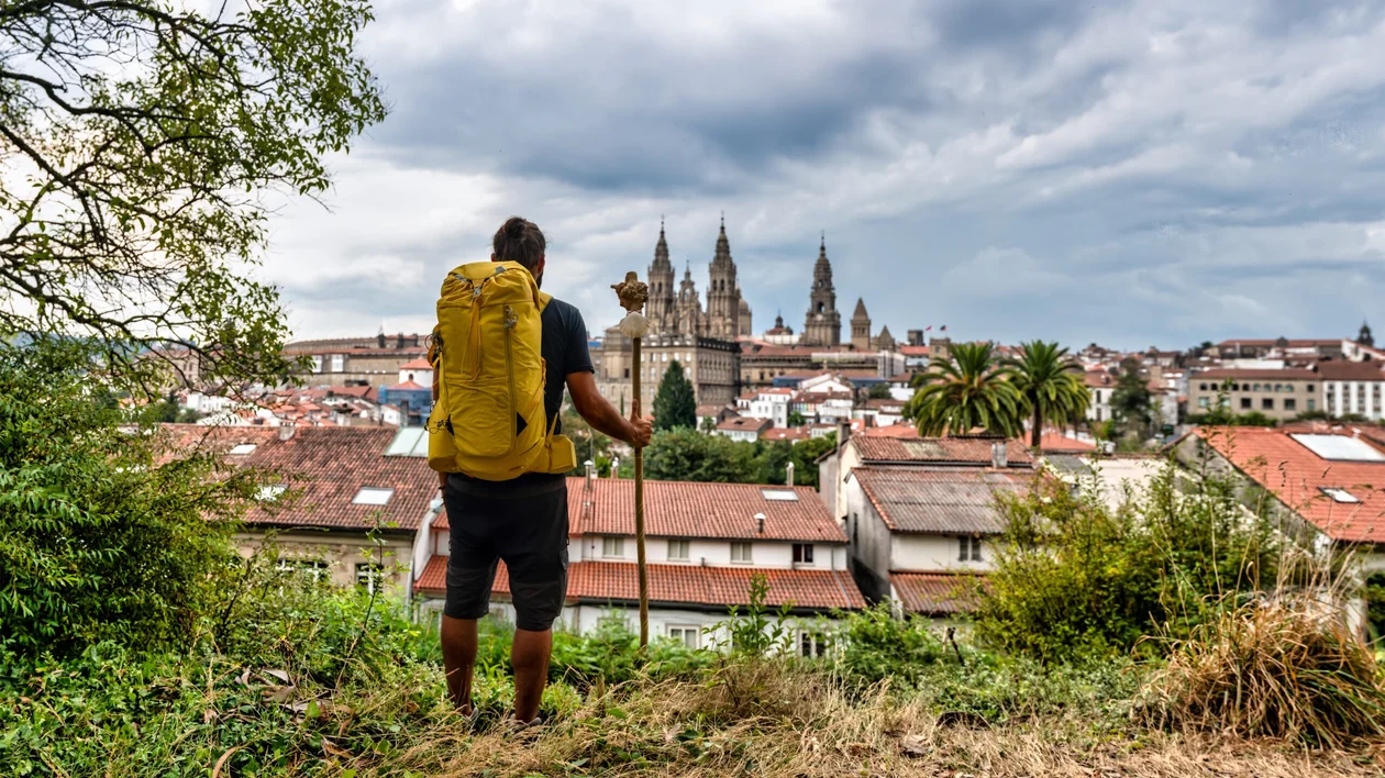 Pilgrims walking along the historic Camino de Santiago trail, surrounded by picturesque landscapes and ancient stone structures, as they make their way towards the shrine of Saint James in Santiago de Compostela, Spain.