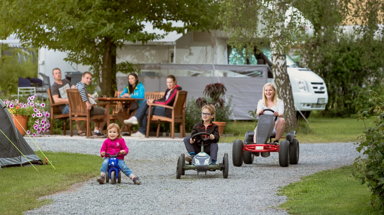 Family camping in the nature: three kids playing and parents in the back having some food with the camping background.