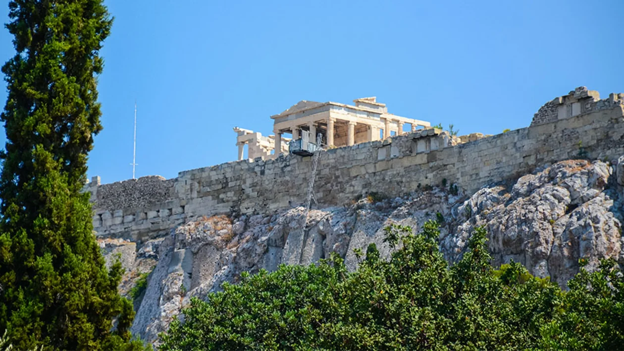 Ancient ruins on a hilltop with green foliage in the foreground against a blue sky.