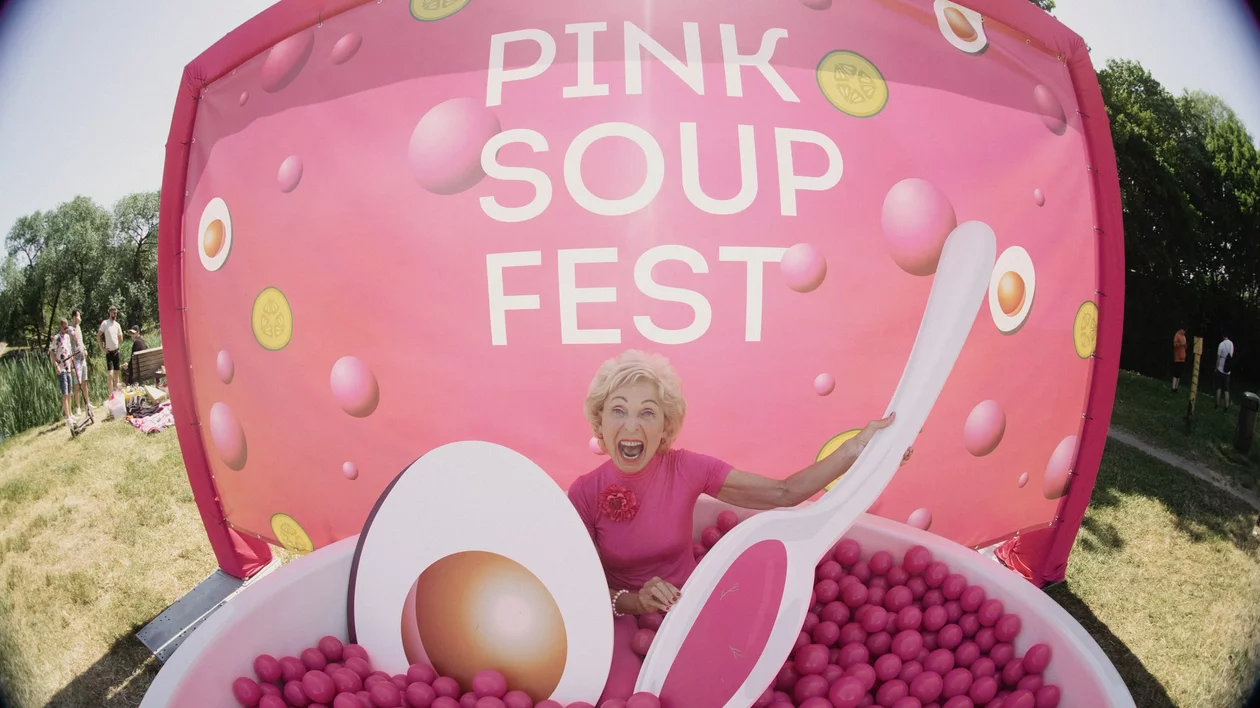 A person inside of a pool filled with pink balls with a background stating Pink soup fest in Vilnius.