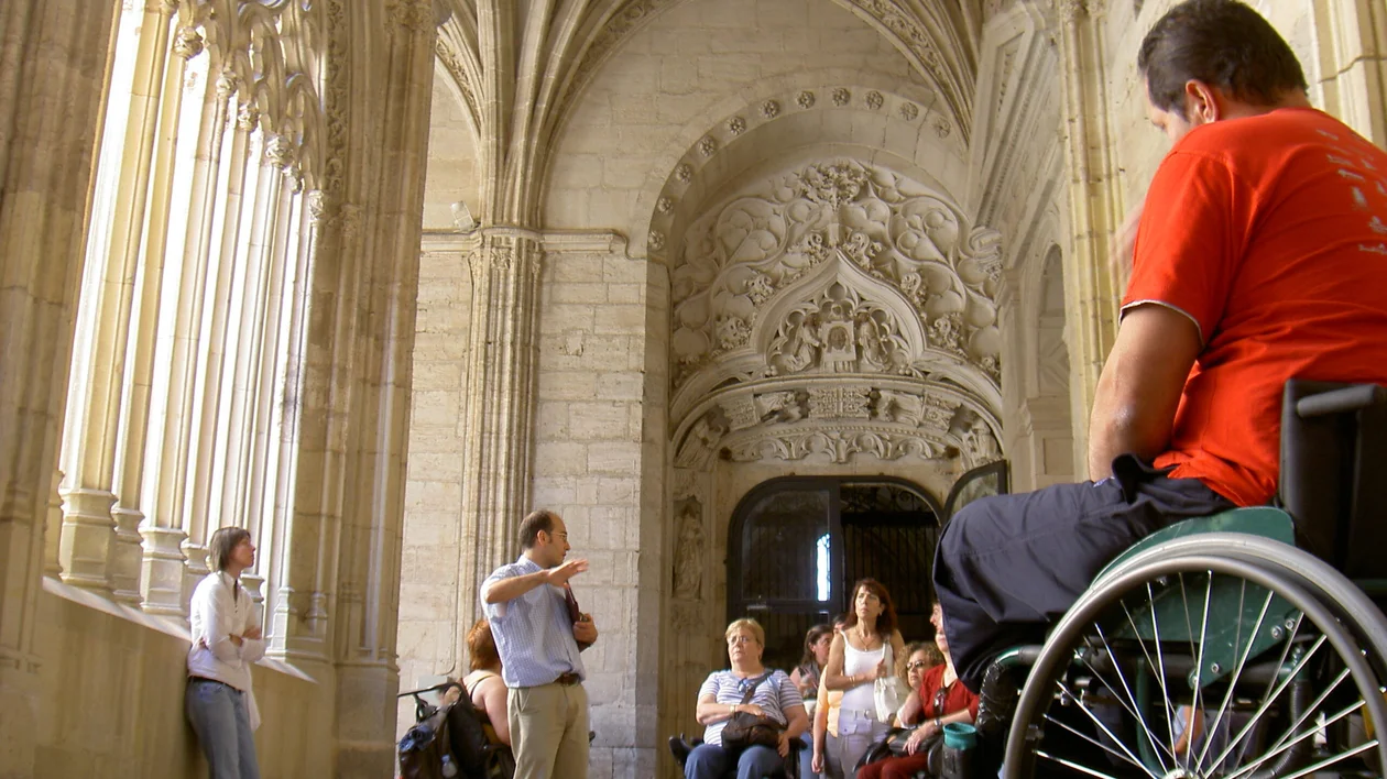 Visitors attending a guided tour in a cathedral with Gothic architecture, some sitting in wheelchairs.