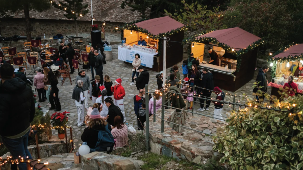 Outdoor Christmas market with festive lights, people browsing stalls and socializing.
