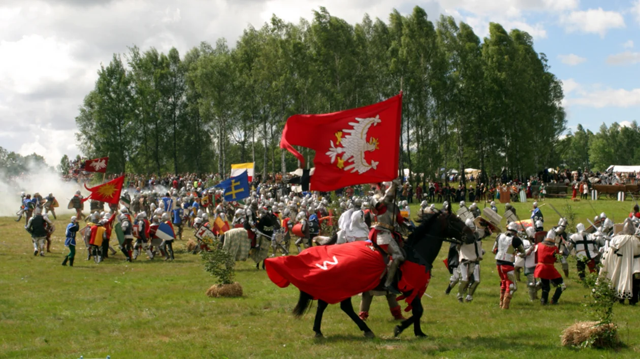 Medieval battle reenactment with knights and flags in an open field at Grunwald.