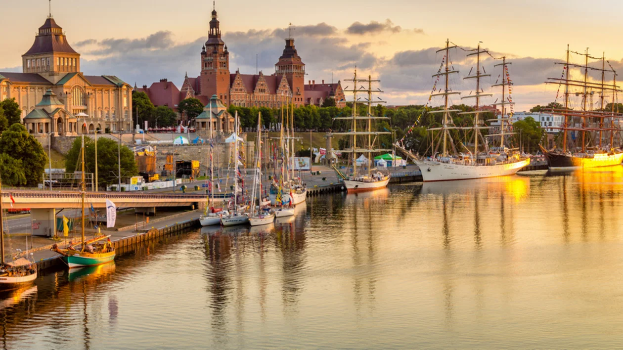 Sunset over a harbor with tall ships and historic buildings in the background in Szczecin.
