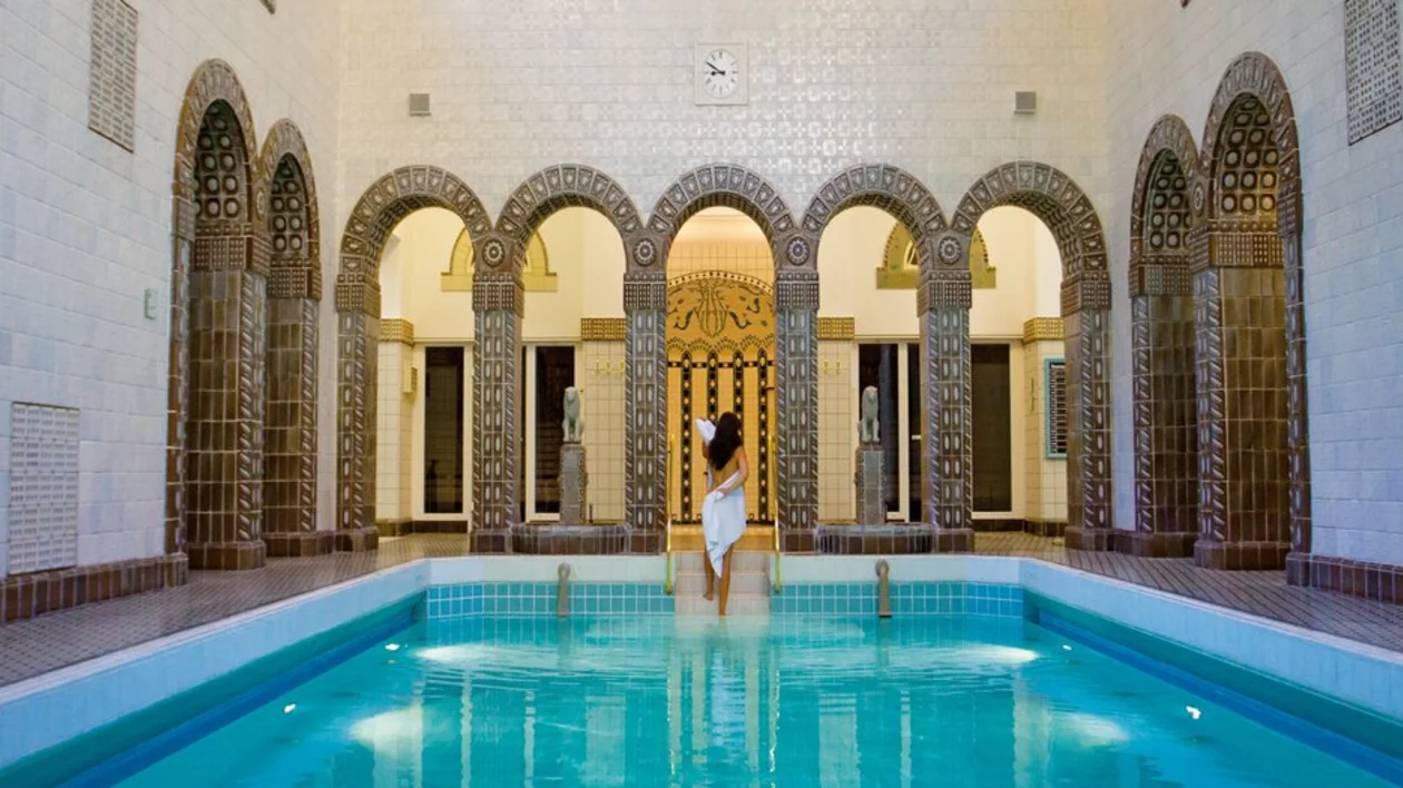 Person by an indoor pool with ornate arches and mosaic tiles.