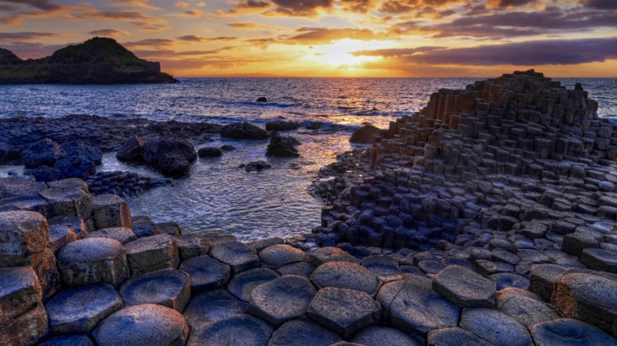 Sunset at a rocky coastline with hexagonal basalt colums and rocks.