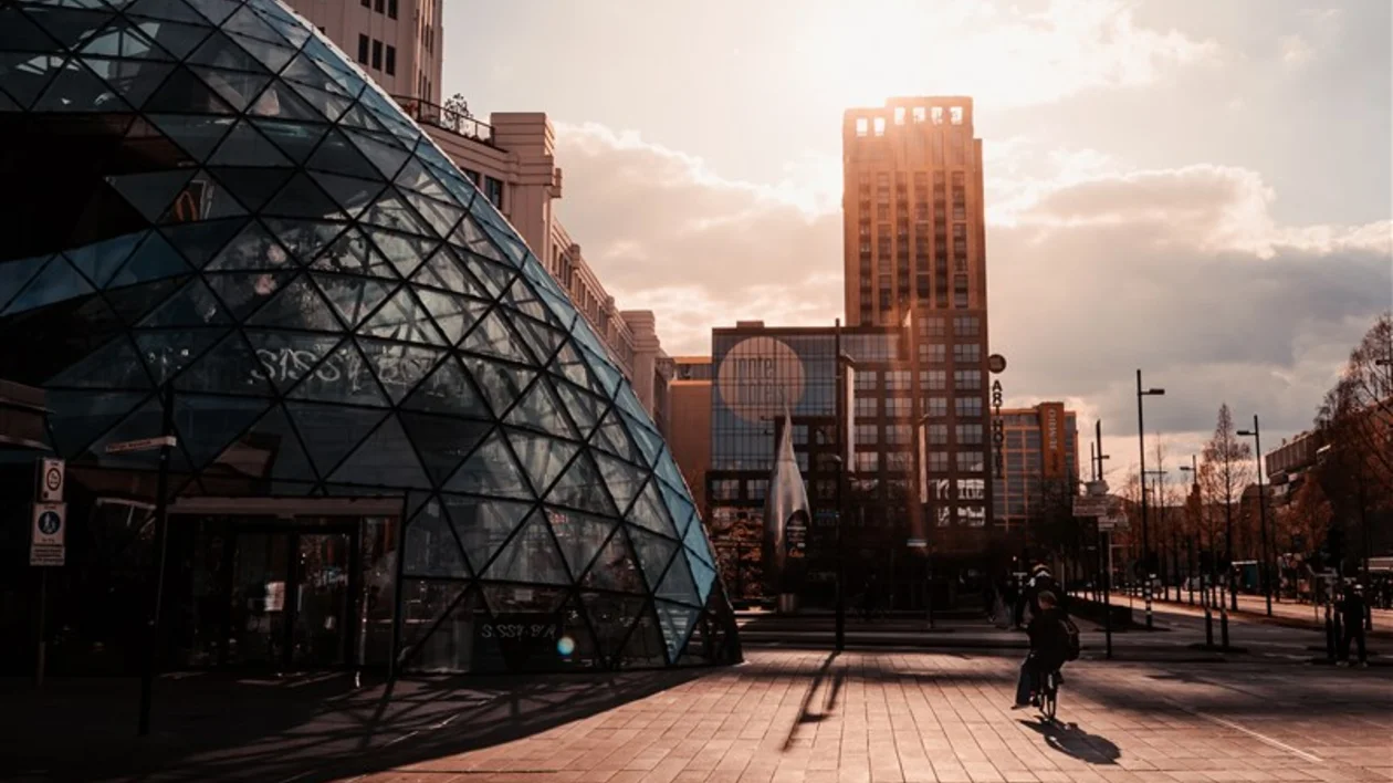 Eindhoven's cityscape with a geometric glass structure and modern buildings at sunset.