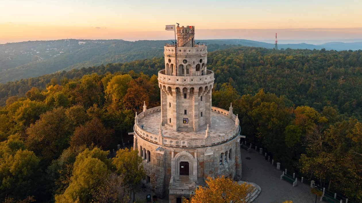 Majestic stone tower of the Erzsébet Lookout surrounded by a the Normafa park with autumn trees, located atop a hill with panoramic views of the surrounding landscape.