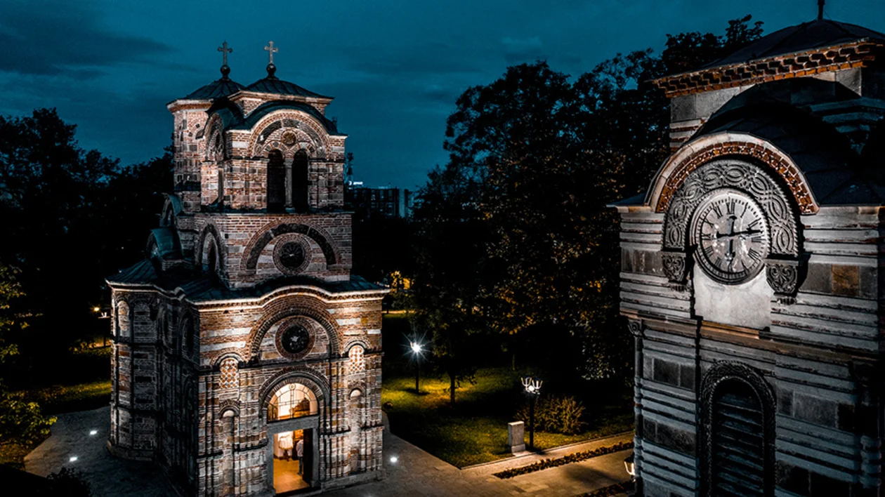 Illuminated brick church and clock tower at night with surrounding trees.