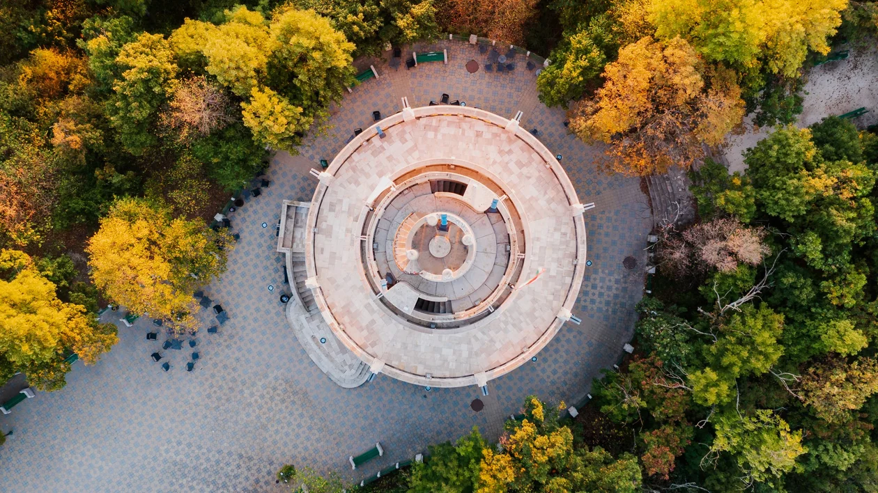 Aerial view of the circular Erzsébet Lookout tower surrounded by green and autumn-coloured trees.