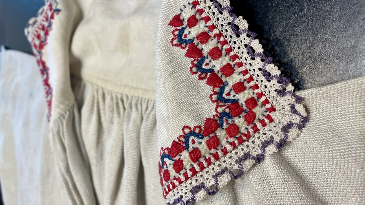 Close-up of traditional handmade embroidery on a beige textile, featuring red, blue, and purple lace details.