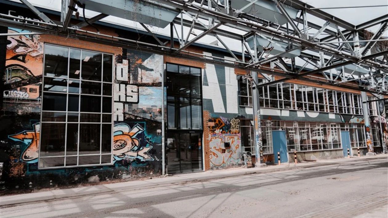 Piet Hein Eek facade adorned with vibrant graffiti art, large windows, and industrial elements under a steel framework.