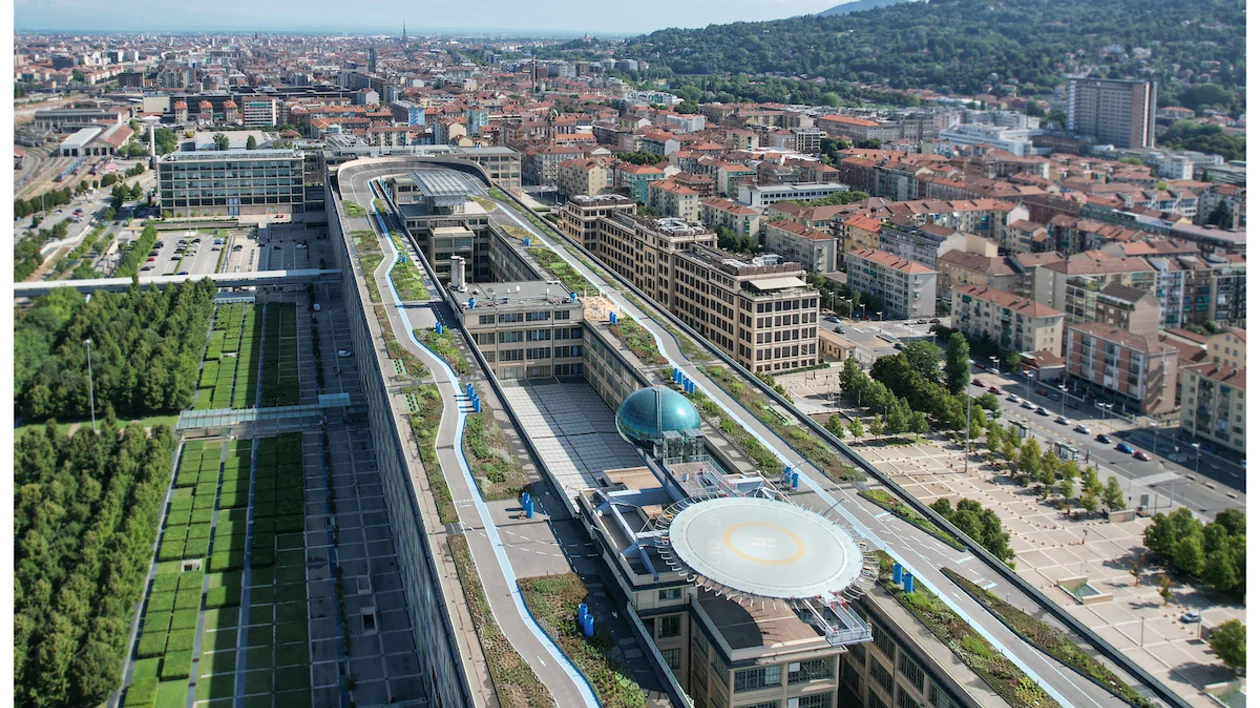 Aerial view of a modern urban landscape featuring green rooftops, buildings, and a helicopter pad, with hills in the background.