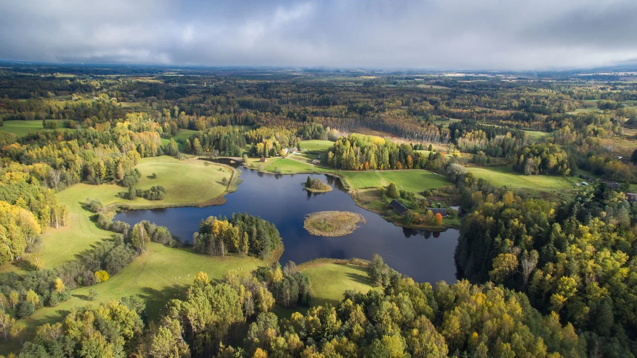 Aerial view of a lush, green landscape featuring a serene lake, scattered islands, and vibrant autumn foliage.