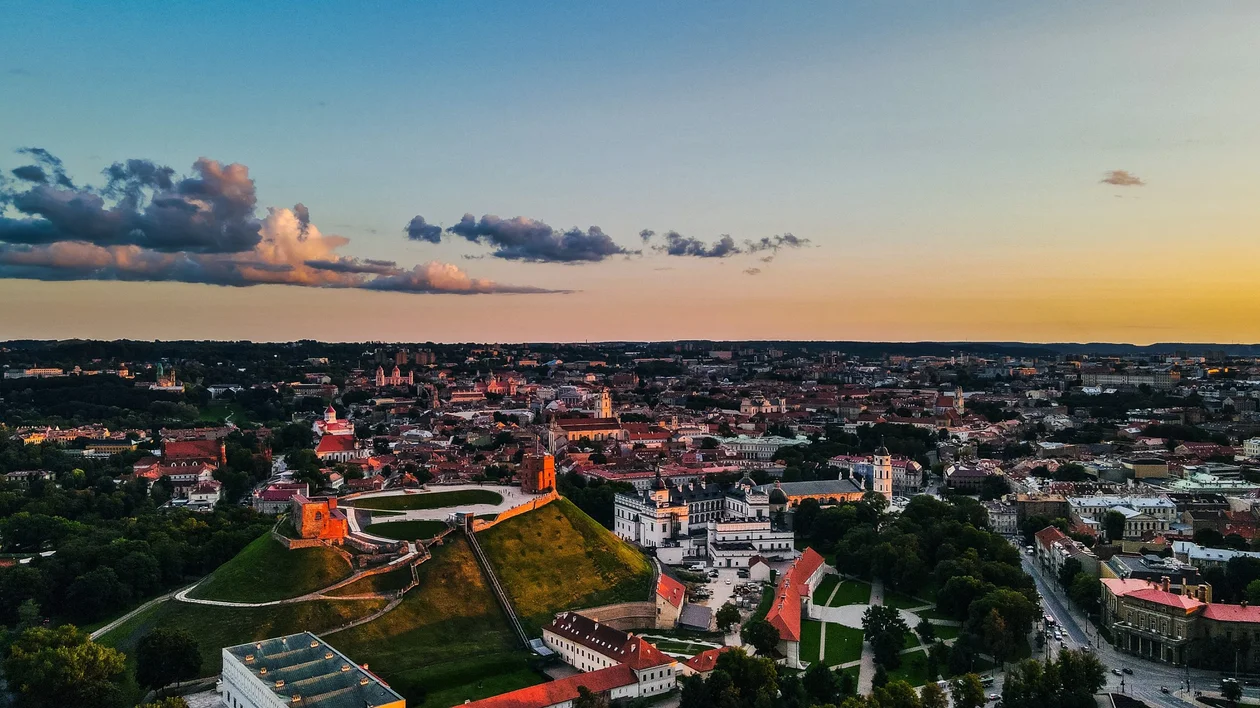 Panoramic view of a Vilnius old town with colourful buildings, a tall church tower, an ornate orthodox cathedral, and modern cityscape in the background.