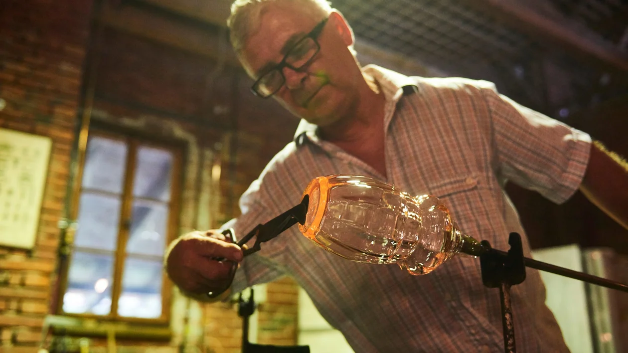A skilled artisan crafting a glass vessel in a traditional glassmaking workshop, surrounded by warm, rustic ambiance.