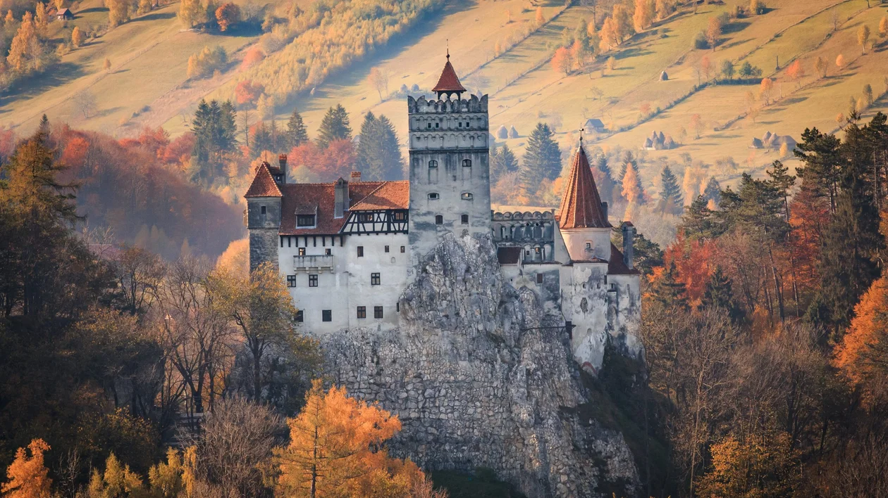 Bran Castle in Transylvania surrounded by vibrant autumn foliage, standing majestically against a backdrop of rolling hills.