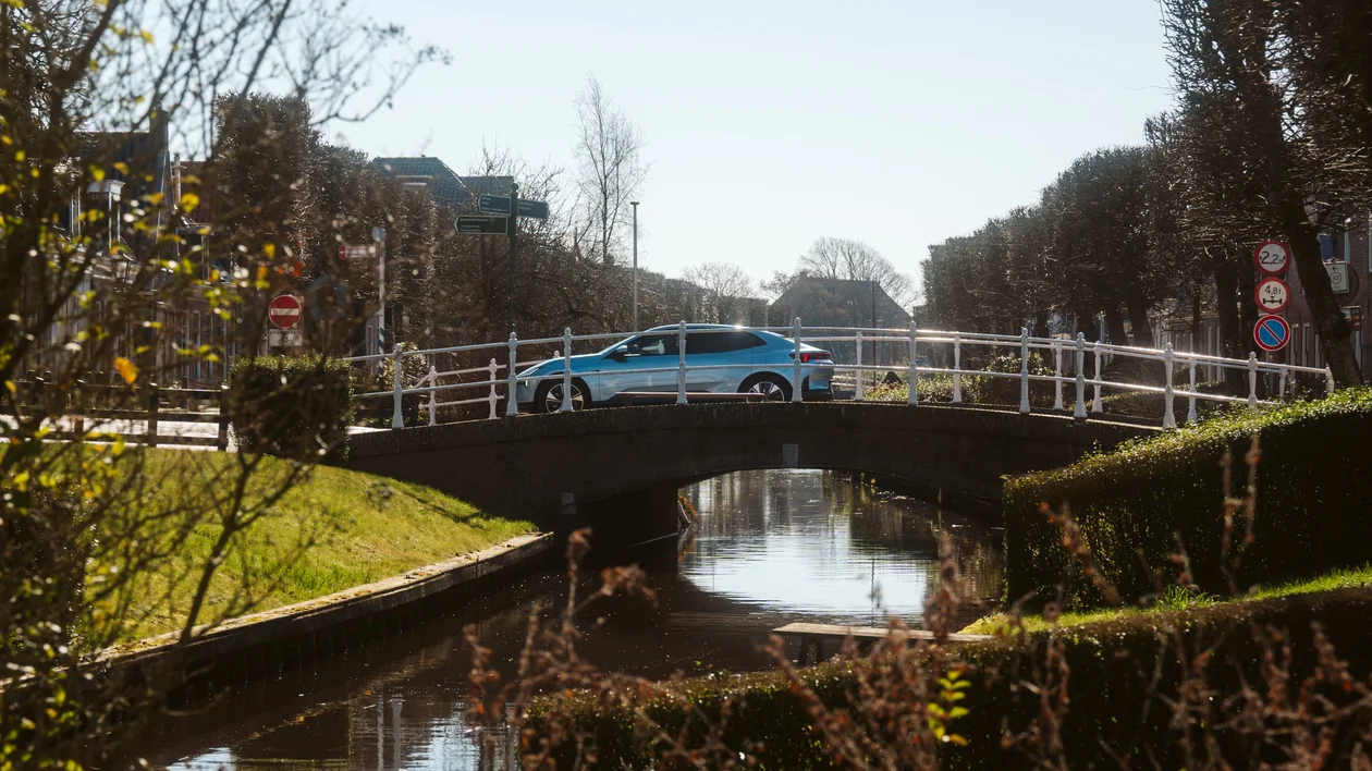 Scenic canal view in IJlst, in the Netherlands, featuring traditional Dutch houses, a wooden footbridge, and lush greenery.