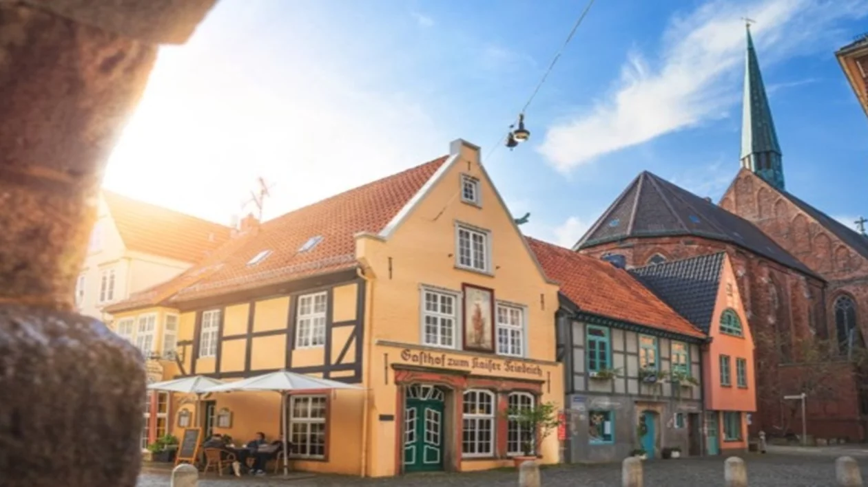 Charming historic buildings with colorful facades and a tall church spire under a bright blue sky in a quaint town square.