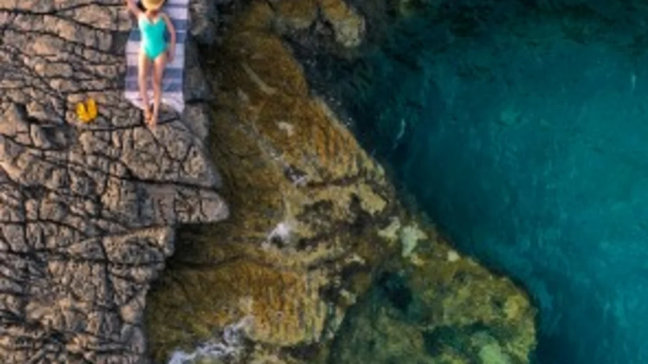 A woman sunbathing on rocky cliffs beside the crystal-clear turquoise waters of Cape Veslo, Montenegro.