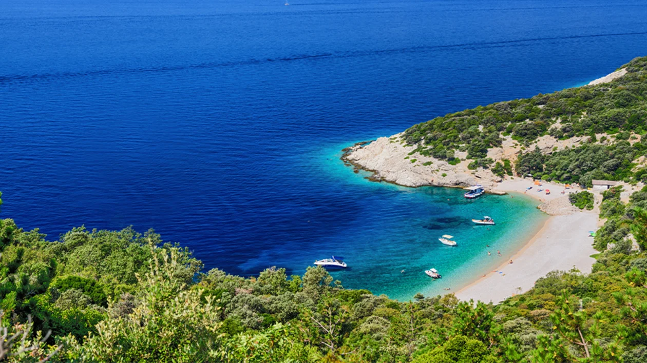 Secluded cove with crystal-clear water and boats anchored by the shore.