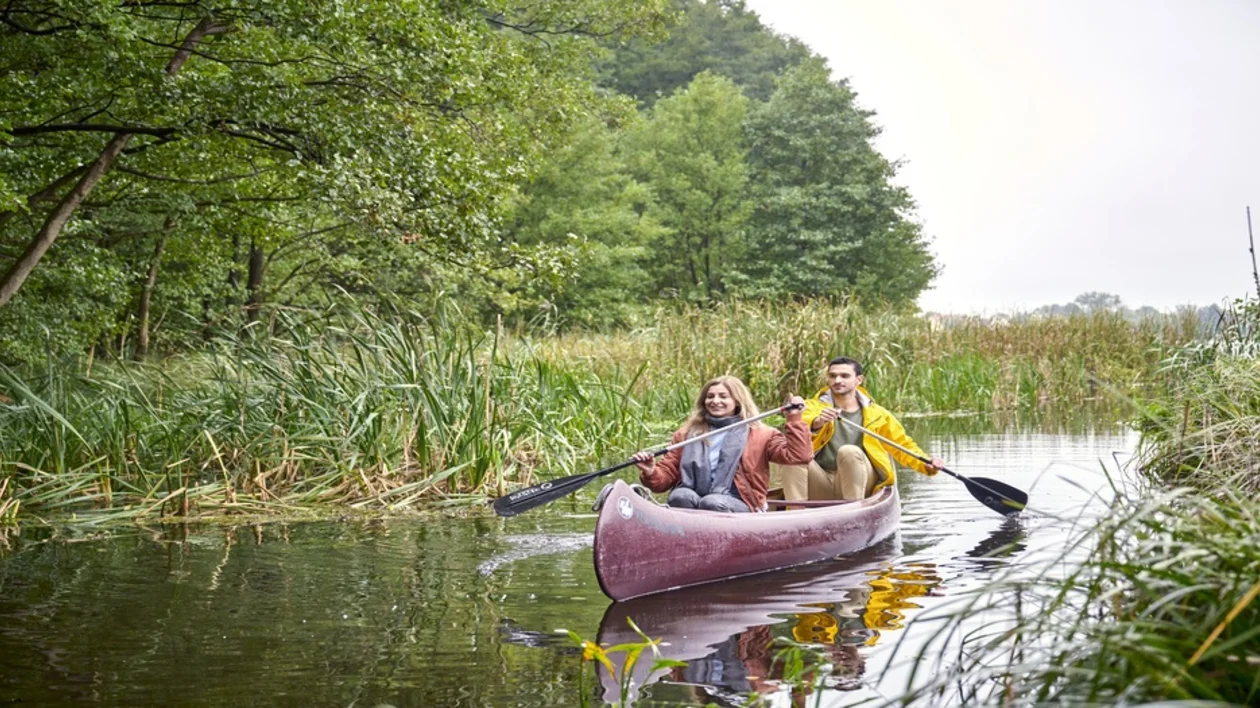 Couple canoeing through a narrow waterway surrounded by lush greenery in Mecklenburg-Vorpommern, Germany.
