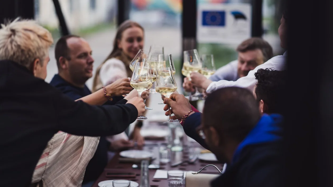 Group of friends toasting Estonian white wine at a long outdoor table in Tallinn.