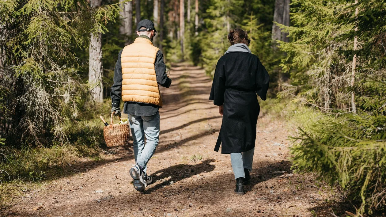 Couple walking through a pine forest trail with a picnic basket of Estonian wine.