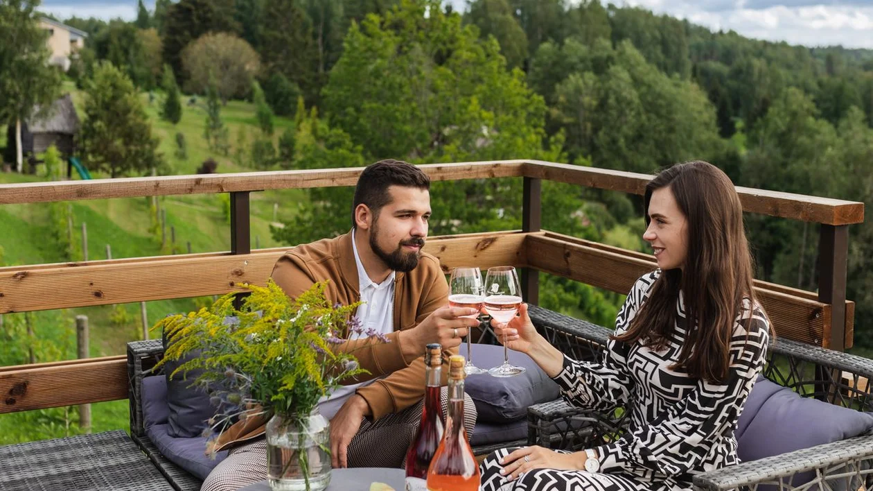 Couple enjoying rosé wine and snacks on the terrace of Murimäe Wine Cellar, surrounded by rolling hills.