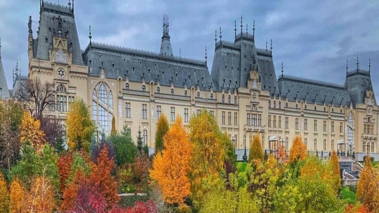 A grand historic building with a symmetrical façade, surrounded by vibrant autumn foliage under a cloudy sky.
