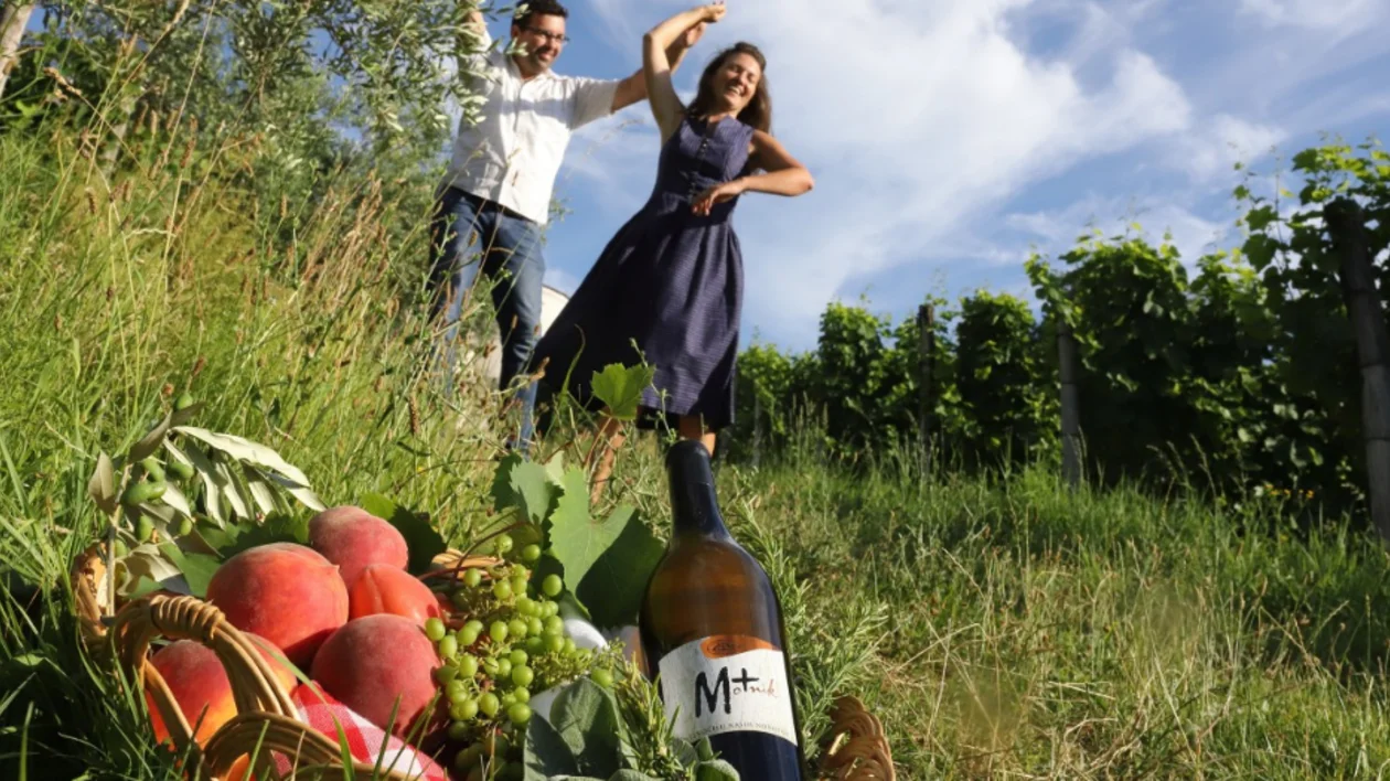 Couple dancing among vineyards in Slovenia with wine, peaches, and grapes in the foreground.