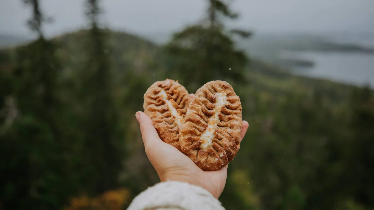 A hand holds two heart-shaped pastries against a backdrop of lush green hills and a misty sky.