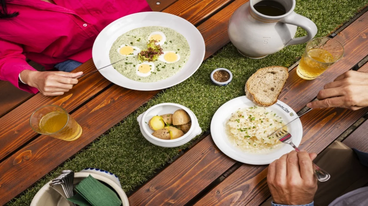 Traditional German cuisine served outdoors with creamy soup, boiled potatoes, sauerkraut, bread and beer on a wooden table.