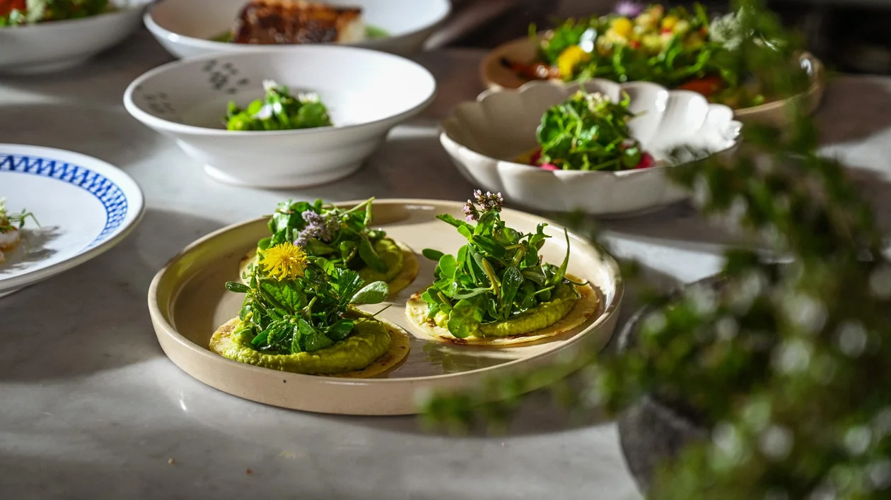 Close-up of a gourmet dish topped with fresh greens and edible flowers, served at a Slow Food-inspired dining event.