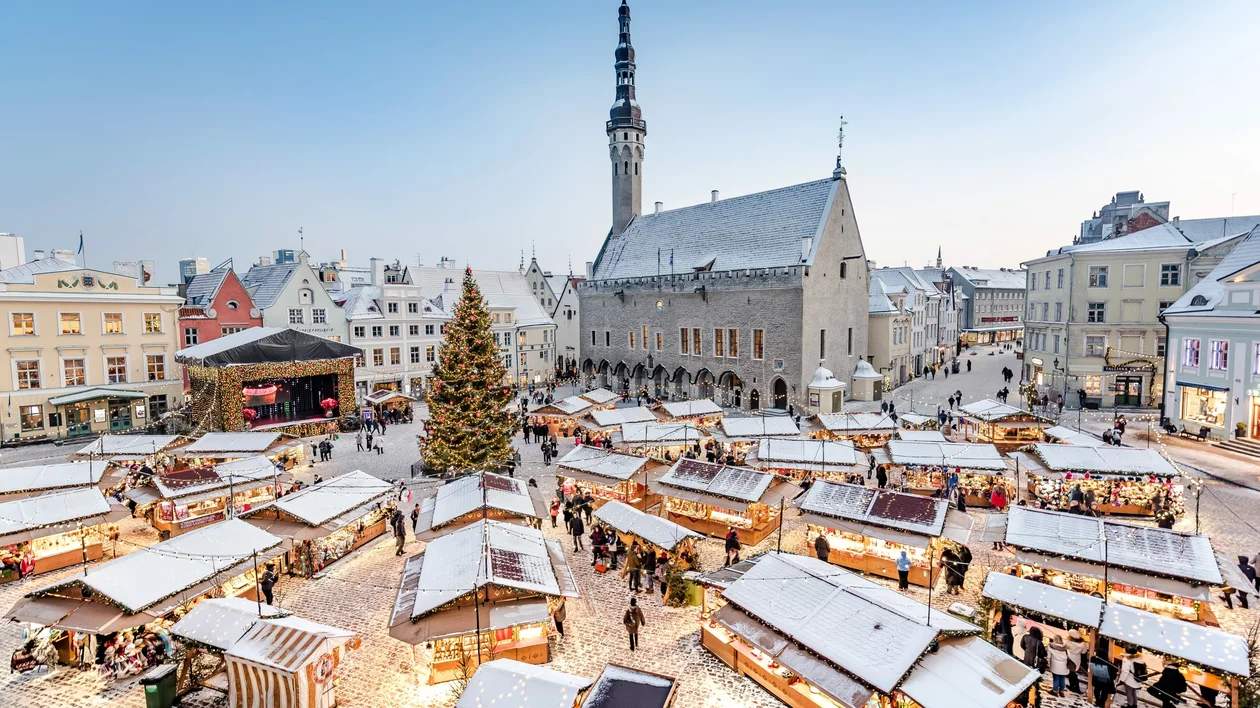 Tallinn Christmas Market in Town Hall Square, Estonia, with snow-covered stalls, festive lights, a decorated Christmas tree, and the historic Town Hall tower in winter.