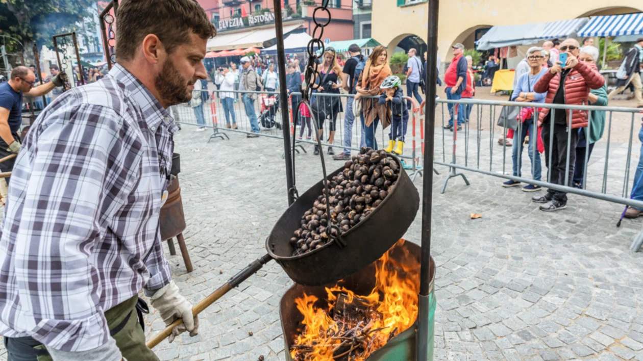 Traditional chestnut roasting at a local festival, with a man preparing chestnuts over fire and a tourist capturing the moment.