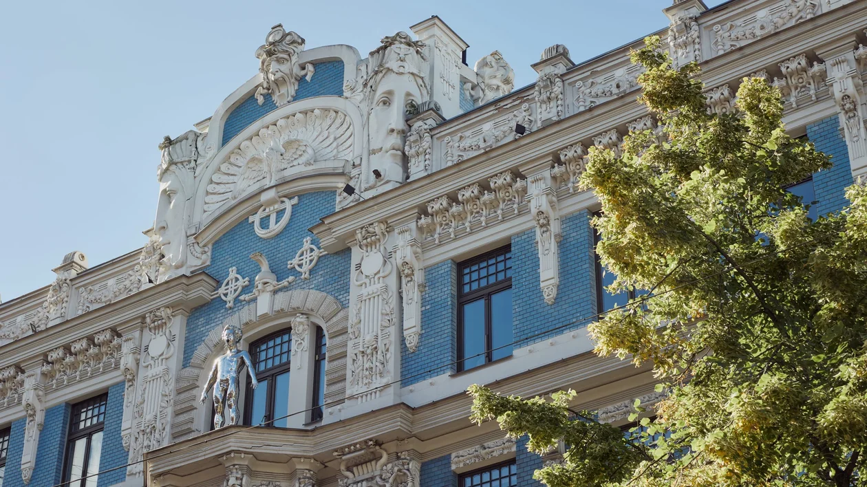 Close-up of an ornate Art Nouveau building facade in Riga, Latvia, featuring intricate sculptures and blue brickwork under a clear sky.