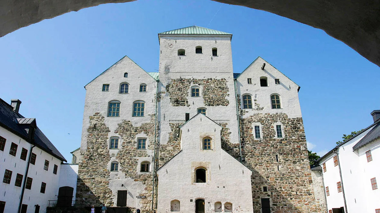 Front view of the medieval Turku Castle on a sunny day, showing its stone walls and towers against a bright blue sky.