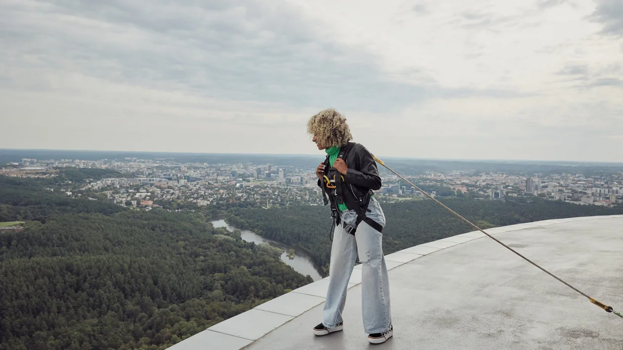 Woman harnessed on the edge of the Vilnius TV Tower, enjoying panoramic views of the city and surrounding forests.