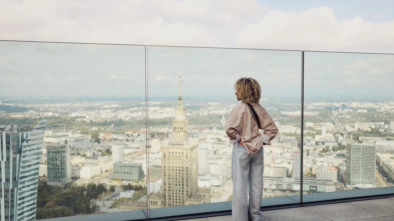 Panoramic view of Warsaw from a rooftop terrace, featuring the Palace of Culture and Science in the foreground.