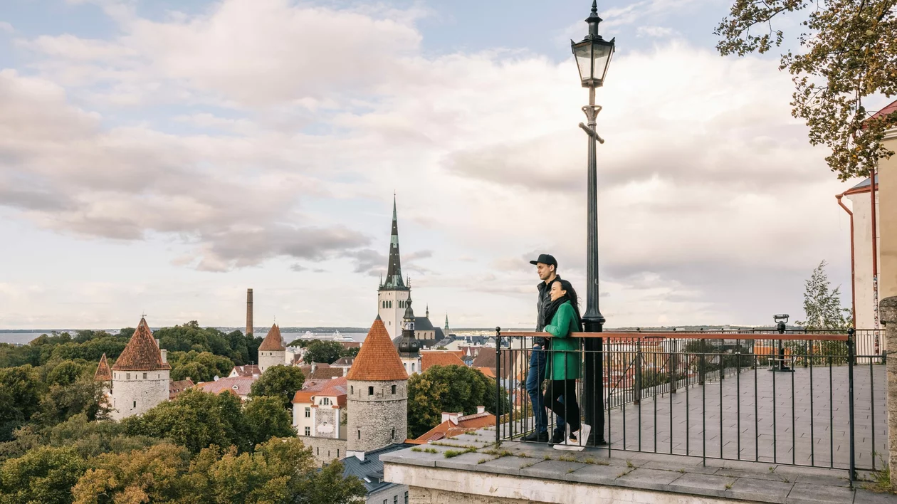 Couple on a viewpoint overlooking the medieval red-tiled roofs and towers of Tallinn Old Town.