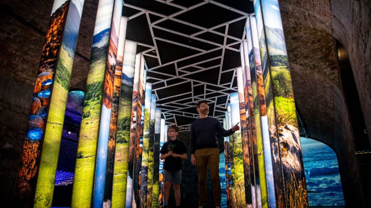 Two visitors walking through EPIC The Irish Emigration Museum in Dublin, surrounded by illuminated panels representing Irish emigration stories.