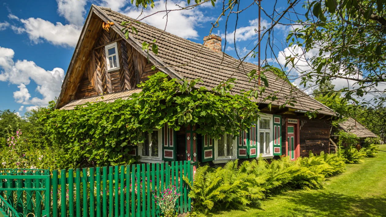Traditional wooden house with colorful open shutters and green garden in the Podlasie region of Poland