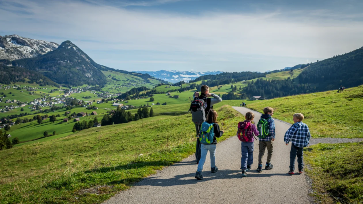 Family hiking on a paved trail through green hills with mountains in the background.