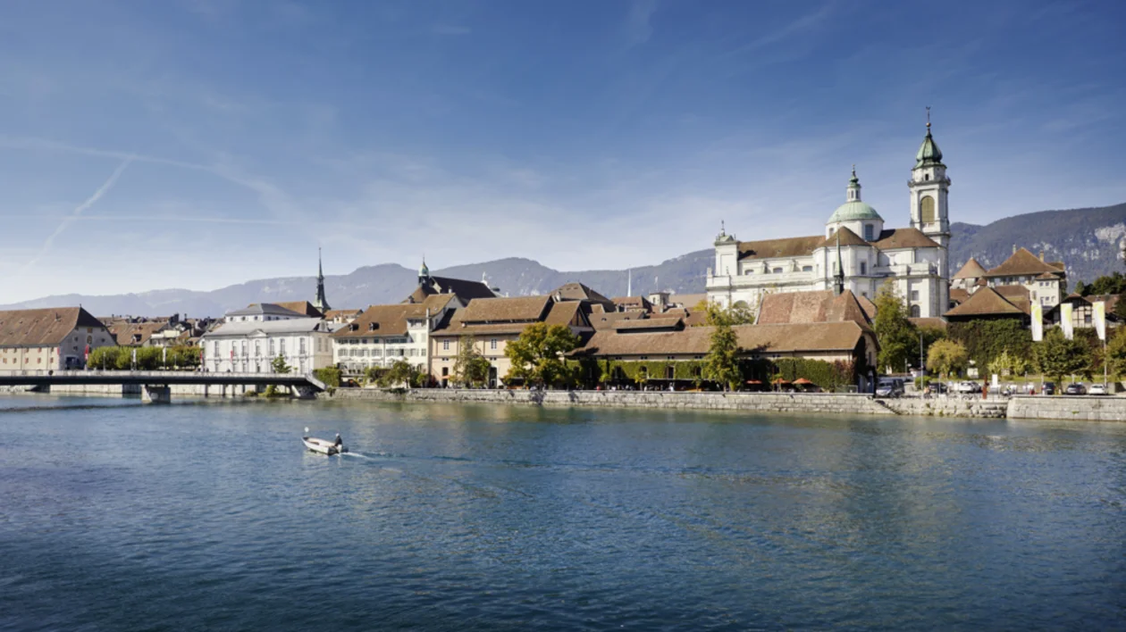 Historic town with domed church beside a calm river under a clear blue sky.