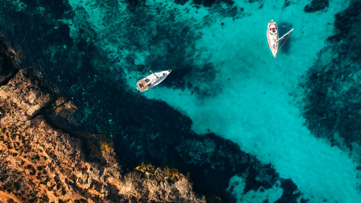 Sailboats anchored in turquoise water near a rocky European coastline