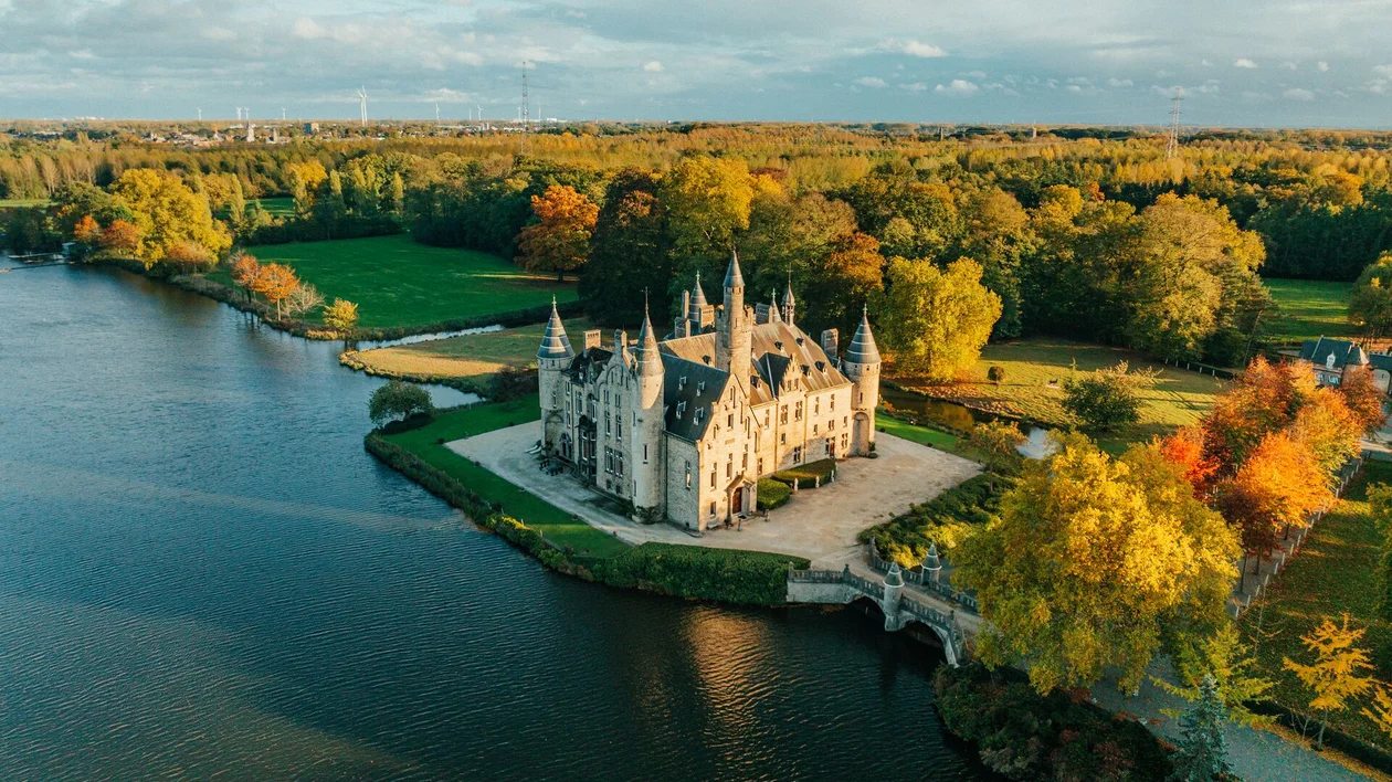 Castle by a lake surrounded by autumn trees under a blue sky.