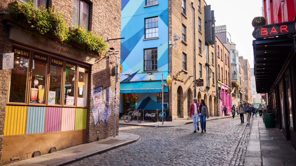 Colourful cobbled street with murals, cafés, and a glowing bar sign