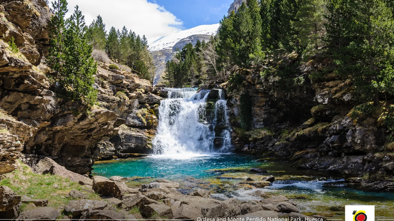 Waterfall cascading into a turquoise pool, surrounded by pine trees and rocky cliffs.