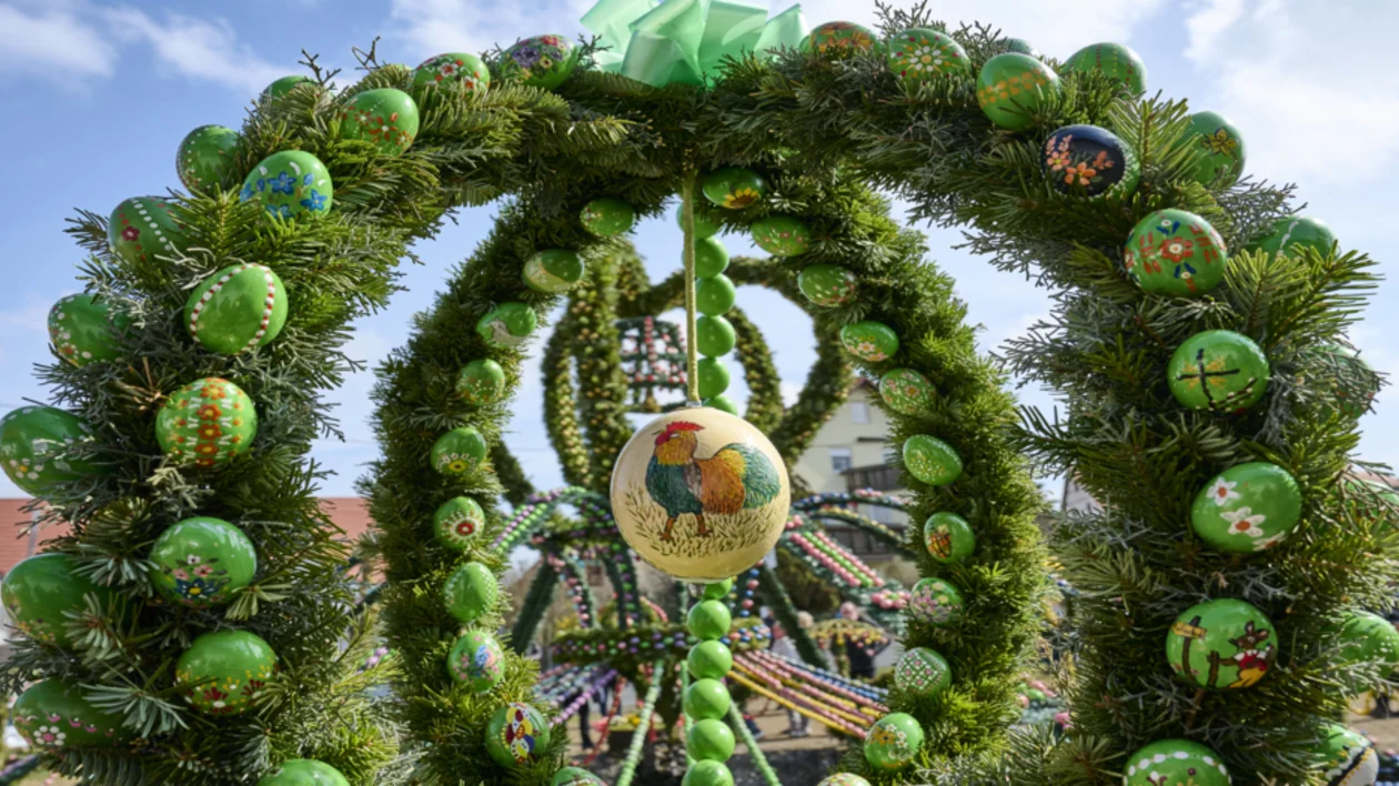 Colorful Easter eggs decorate a green wreath outdoors against a blue sky.